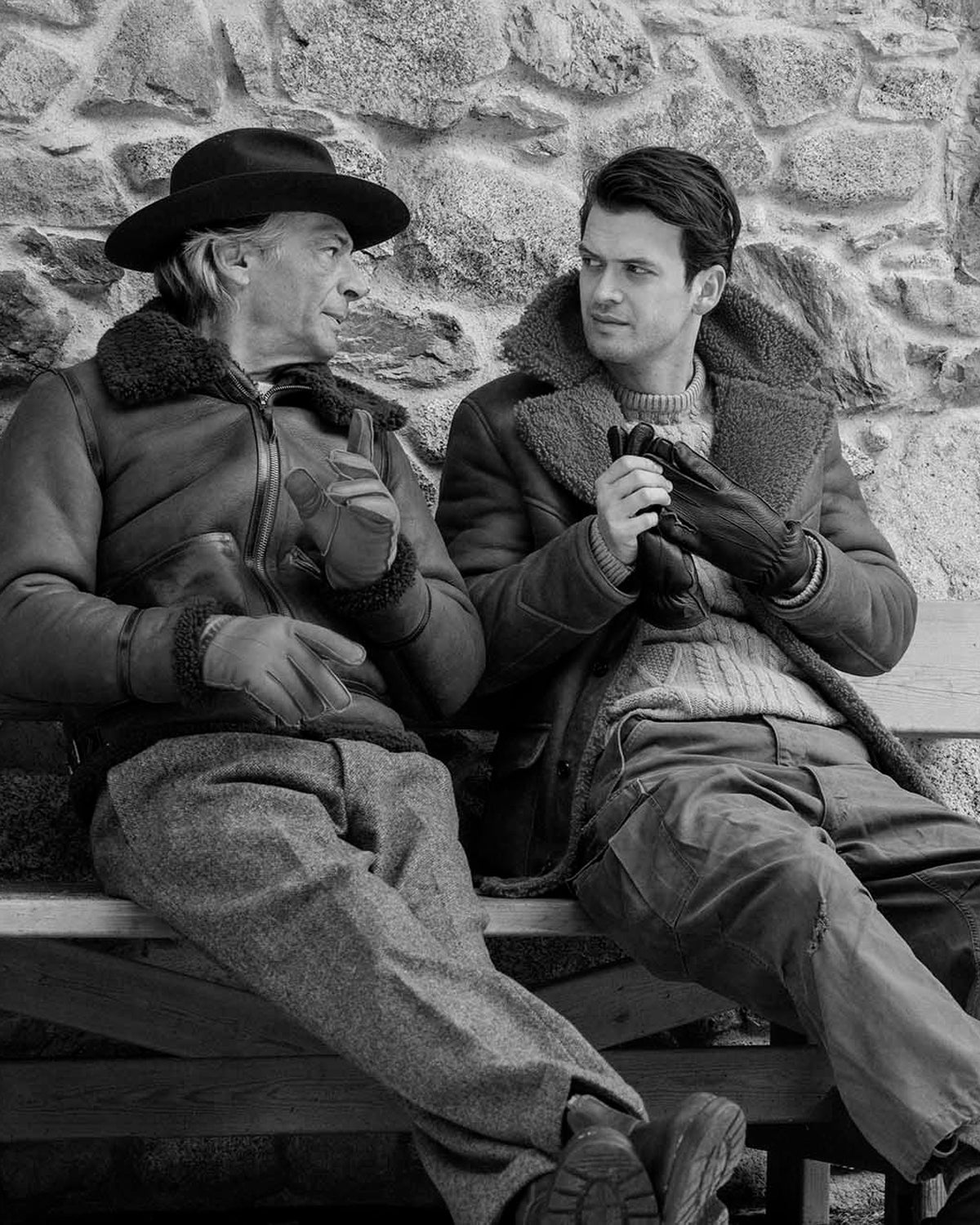 Two Men sitting on a bench while wearing real shearling jackets and leather gloves