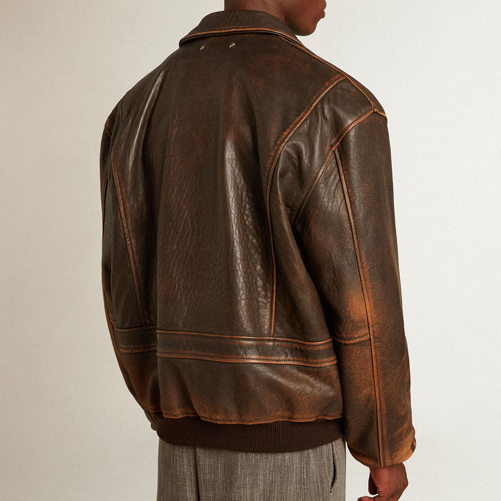 A person shown from the back wearing a distressed brown leather jacket with orange-brown contrast stitching, photographed against a plain light background.