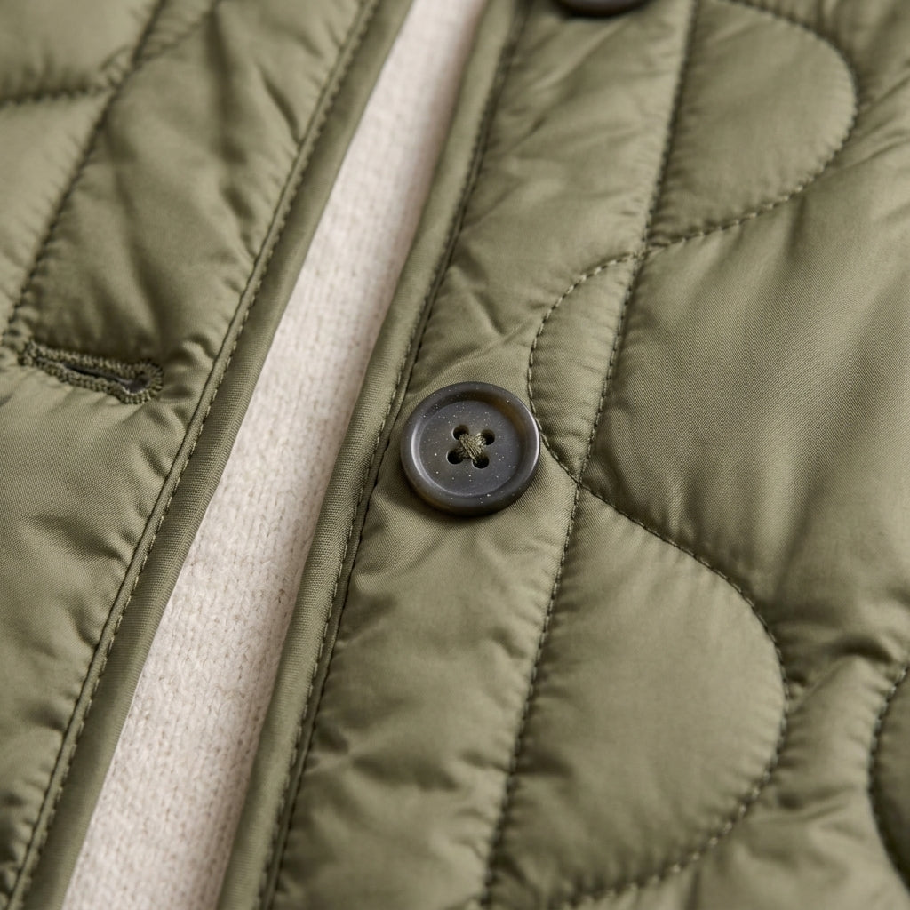 Close-up of an olive green quilted jacket with a dark button and a cream-colored inner lining or underlayer.