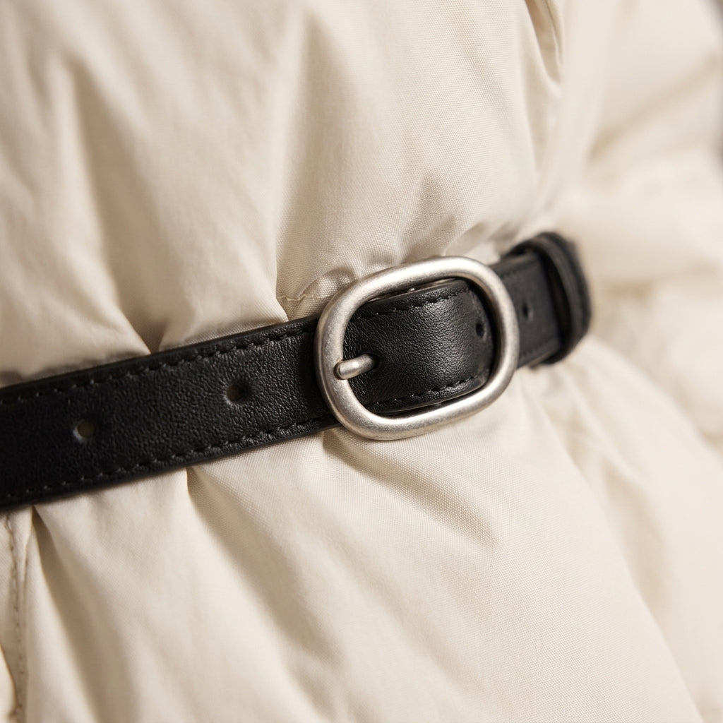 A close-up of a black leather belt with a silver-toned oval buckle, worn around a Quilted White Jacket.
