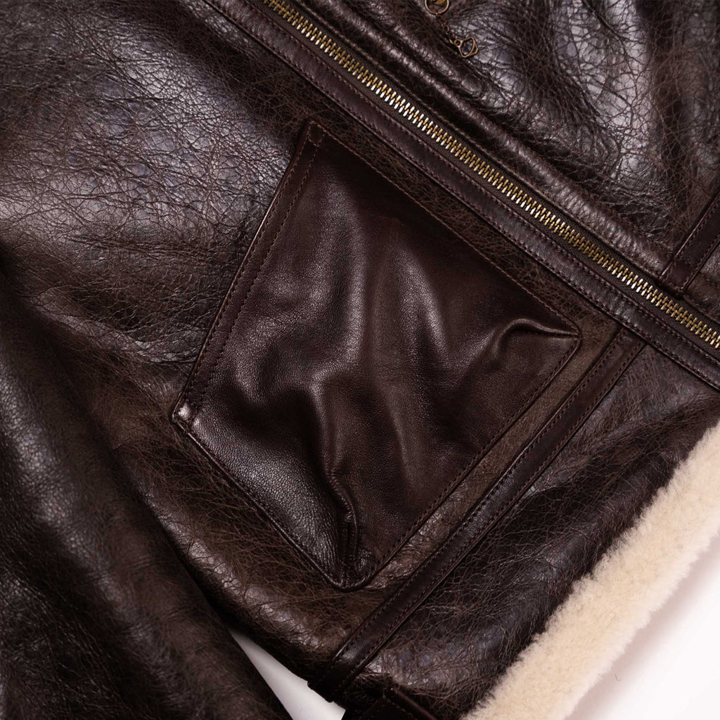 Close-up of a dark brown leather jacket showing a textured leather panel, a gold-toned zipper, and a cream-colored shearling lining.