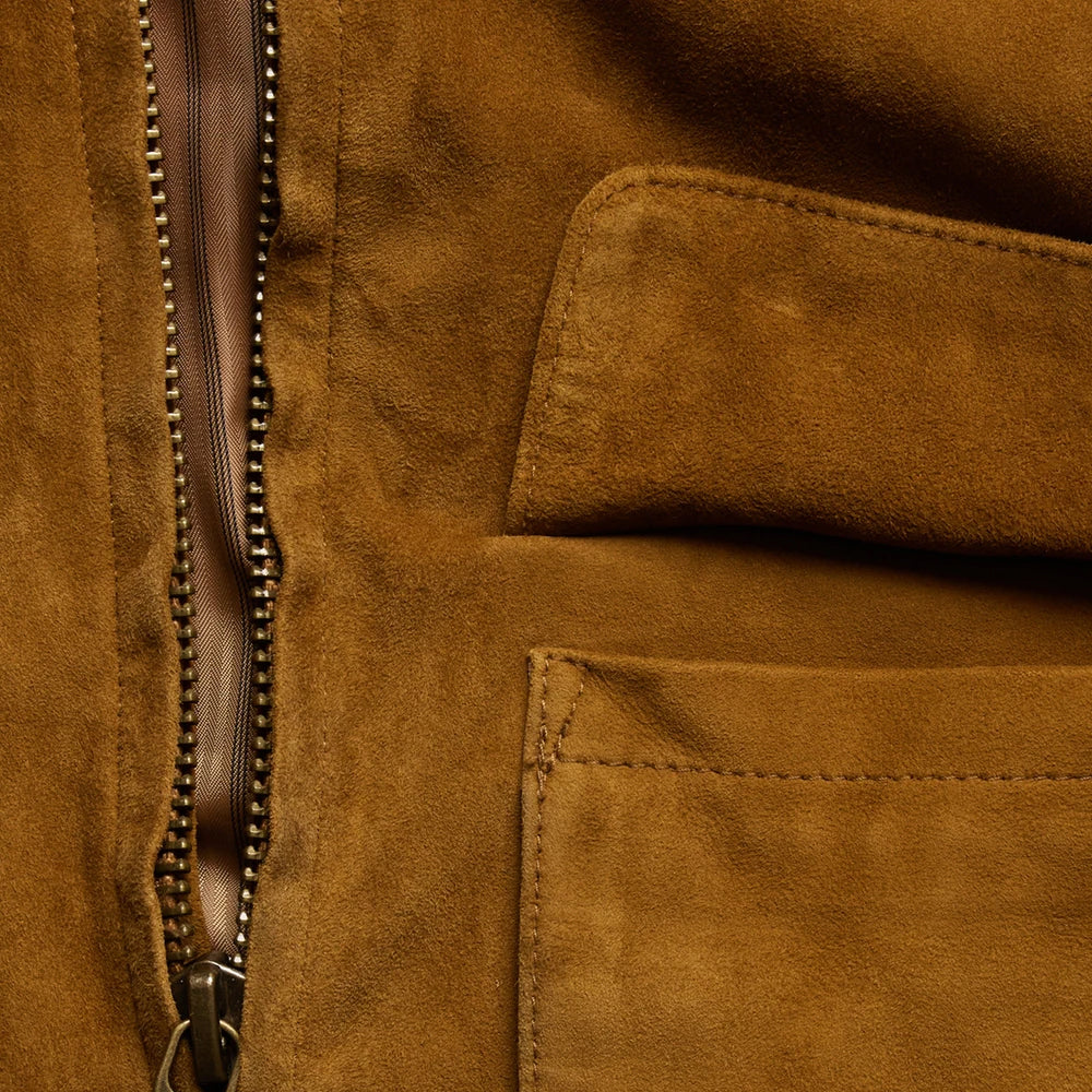 Close-up detail of a brown suede or nubuck jacket, showing a vertical zipper with metallic teeth and a stitched pocket.