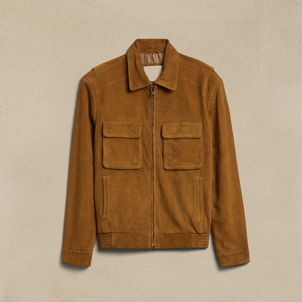 A Suede Men Jacket with a front zipper, two large flap chest pockets, and two vertical welt pockets on the lower front, displayed against a textured beige background.