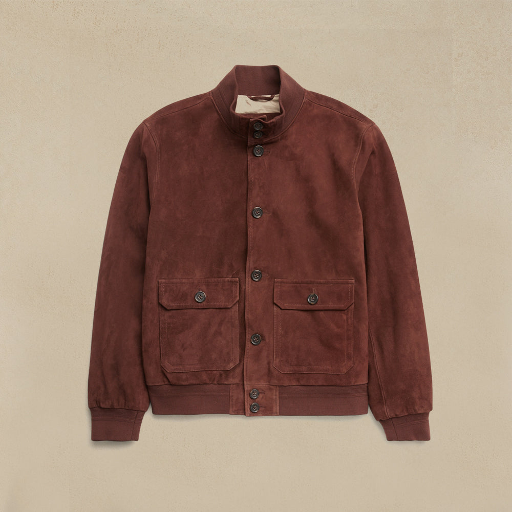 A Men Suede Bomber Jacket with a stand collar, button closure, and two front flap pockets, displayed flat against a textured beige background.