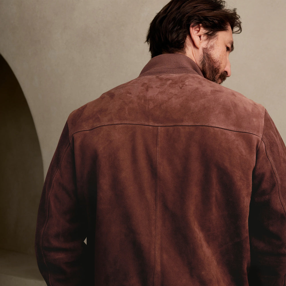 A man viewed from behind wearing a brown suede jacket in a warm, minimalist interior setting.