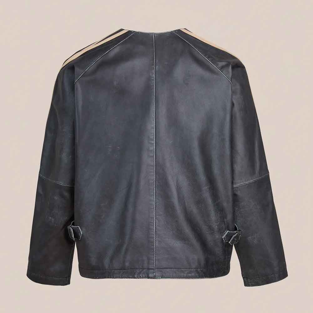 A black leather jacket shown from the back, featuring beige contrast stitching along the shoulders and sleeve cuffs, set against a solid light beige background.