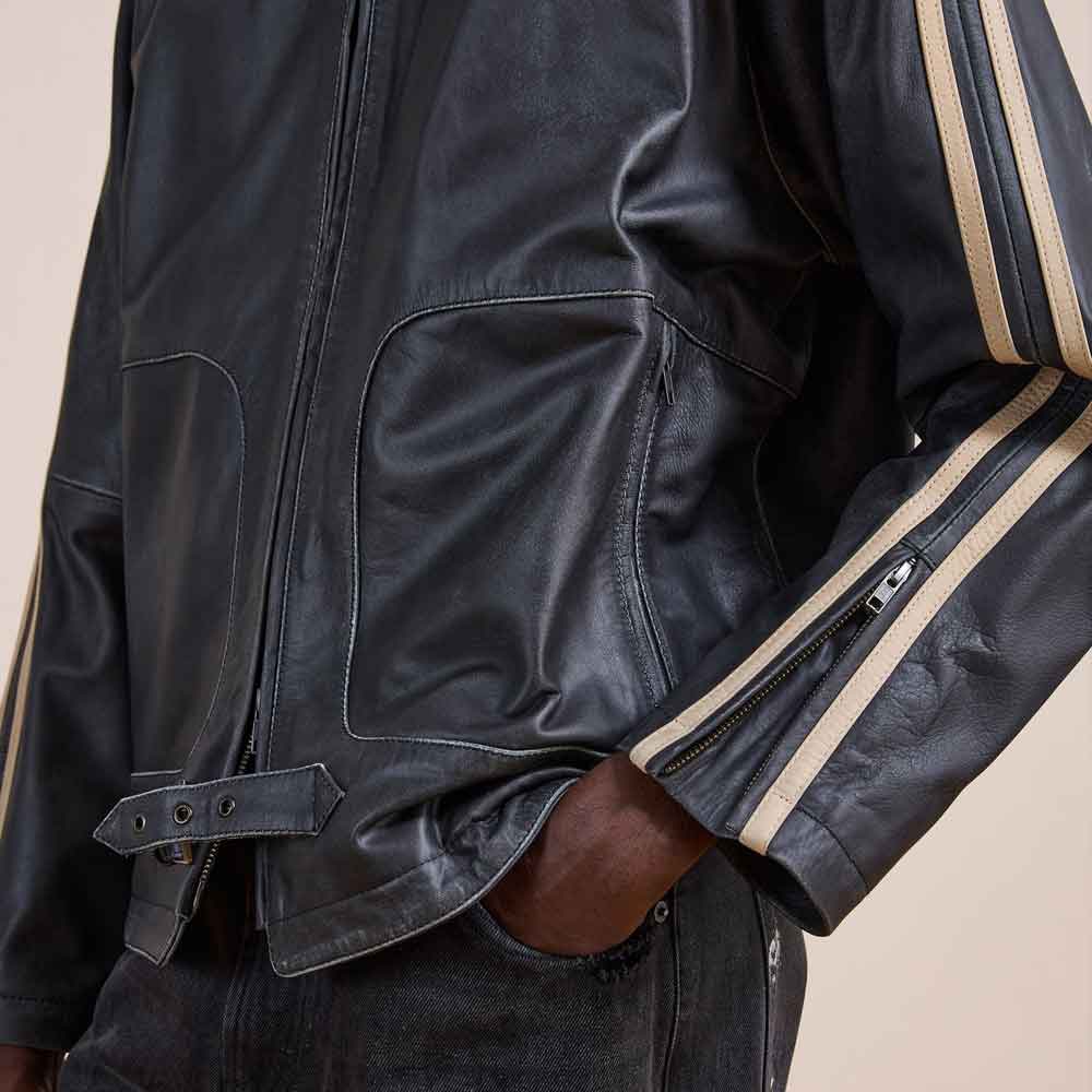 Close-up of a black leather jacket worn by a model, showing the front zip closure, chest pockets, and sleeve details with beige stripes.