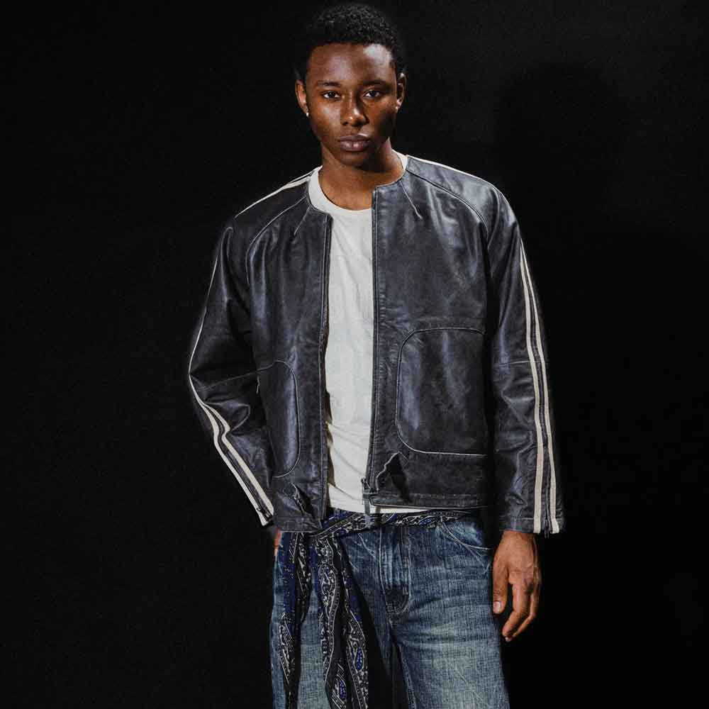 A model wearing a black distressed leather jacket with white stripes on the sleeves, styled over a white t-shirt and blue jeans against a black background.