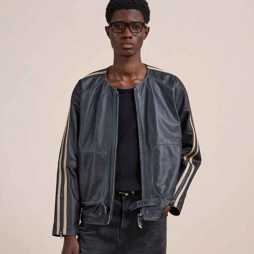 A model wearing a black leather jacket with beige stripes on the sleeves, styled over a black t-shirt and dark jeans against a solid beige background.