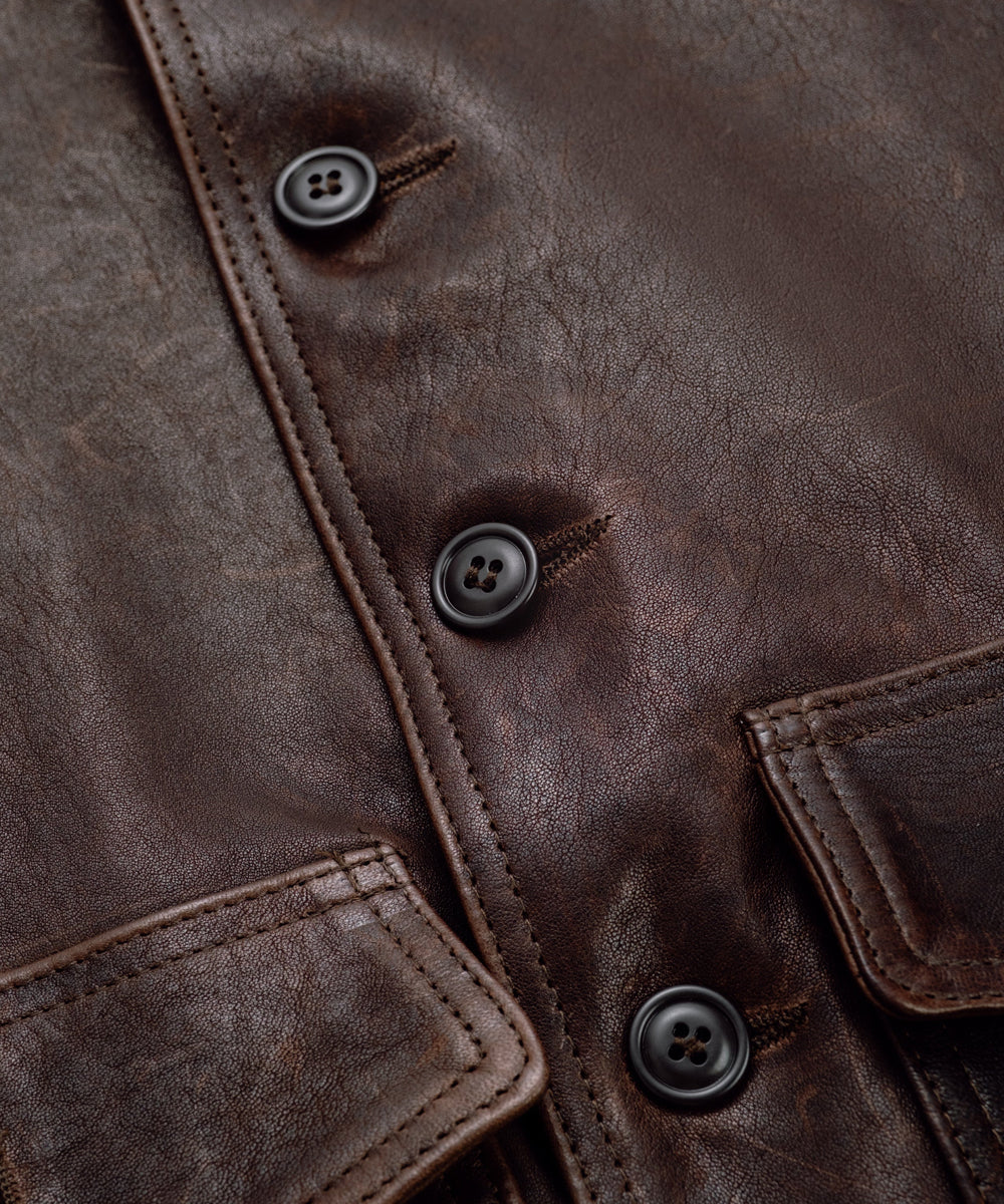 Close-up of a dark brown distressed leather jacket with black buttons and visible raw leather edges.