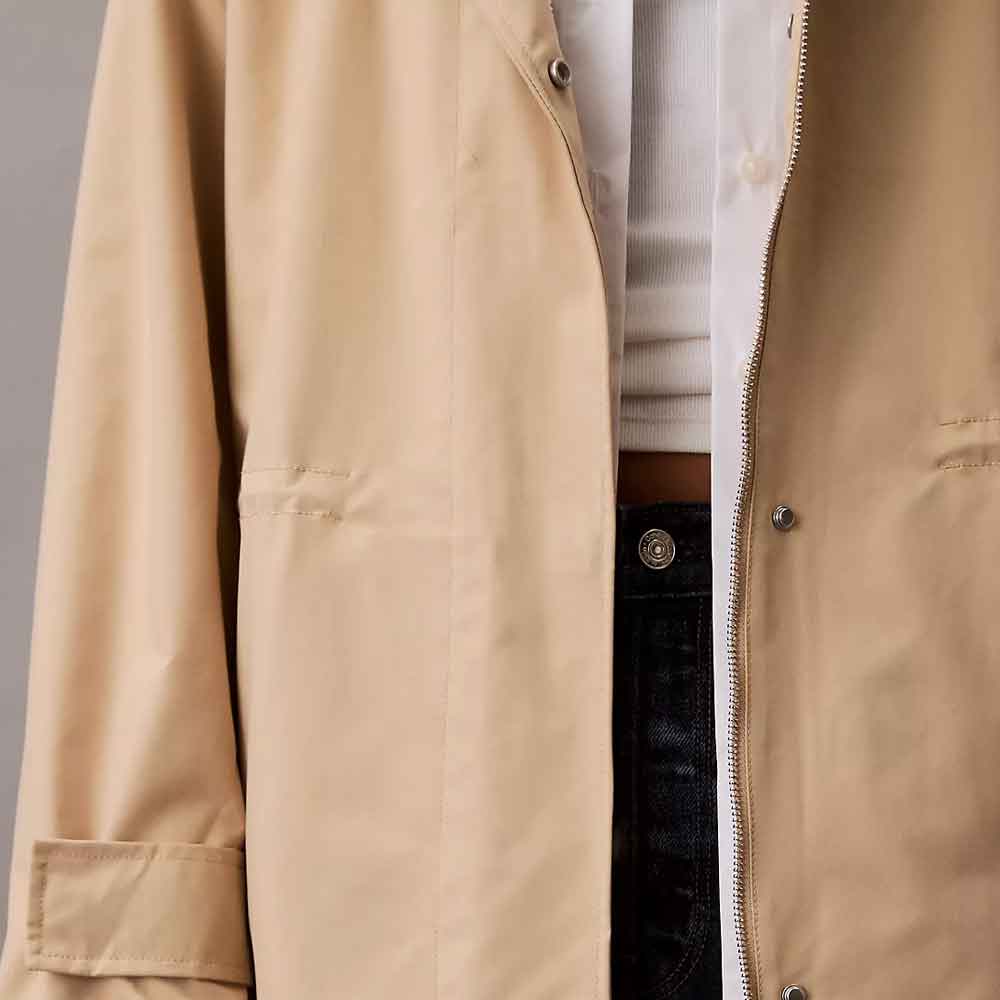 Close-up of a beige Anorak Rain Jacket worn over a white shirt and dark jeans, showing the fabric texture, button details, and zipper.