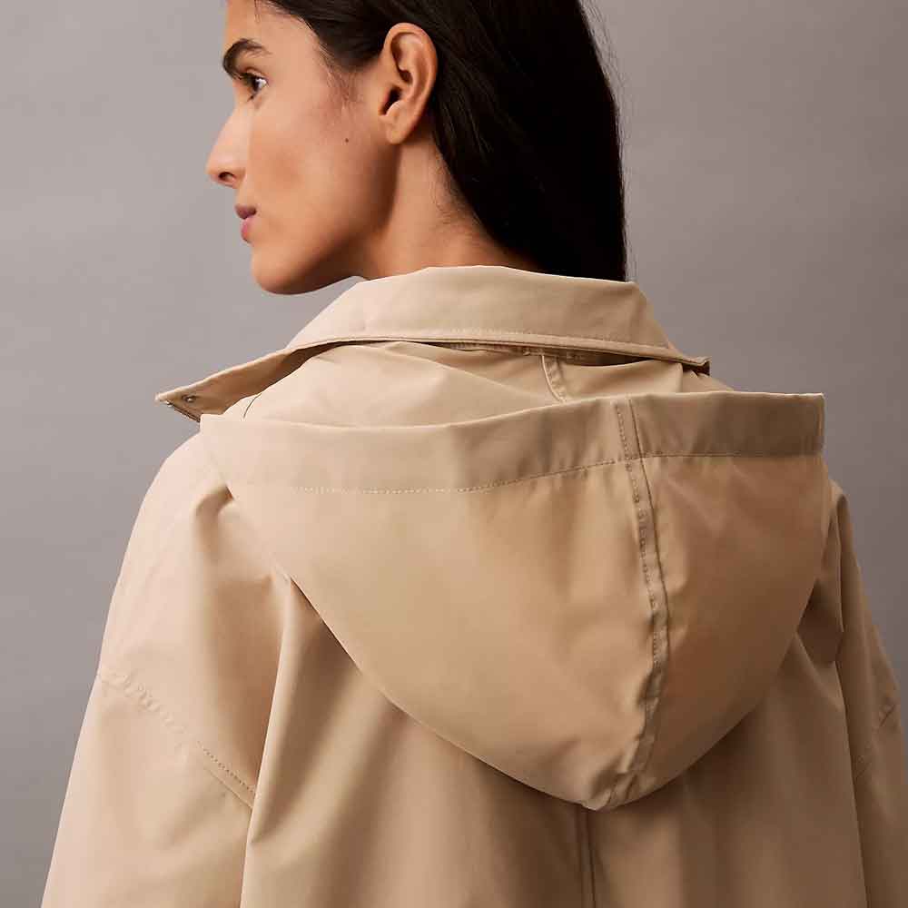 A close-up side profile of a model wearing a light beige hooded Anorak Rain Jacket against a solid gray studio background.