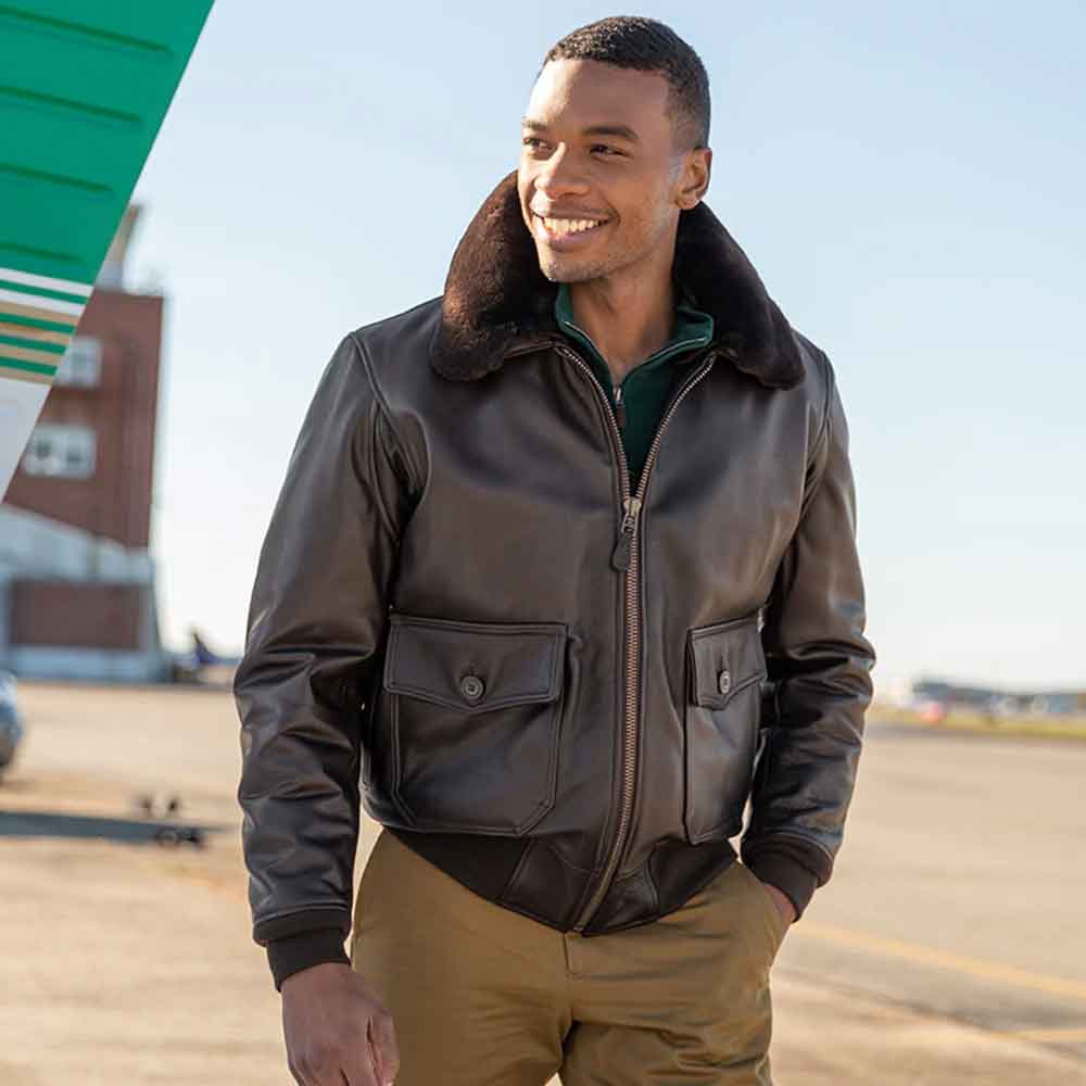 A man wearing a dark brown leather aviator-style jacket with a brown faux-fur collar, standing outdoors on an airfield.