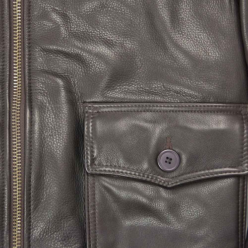 Close-up of a dark brown pebbled leather jacket featuring a front flap pocket with a matching gray button and a gold-toned zipper on the left side.