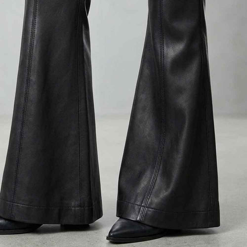 Black leather flare pants shown from the knees down, worn with black pointed-toe shoes on a light gray studio floor.