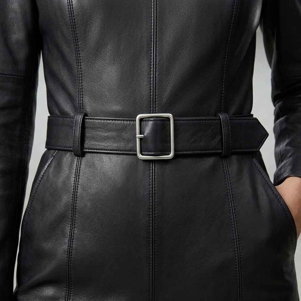 Close-up of a black leather belt with a square silver buckle worn at the waist over a black leather jacket or dress.