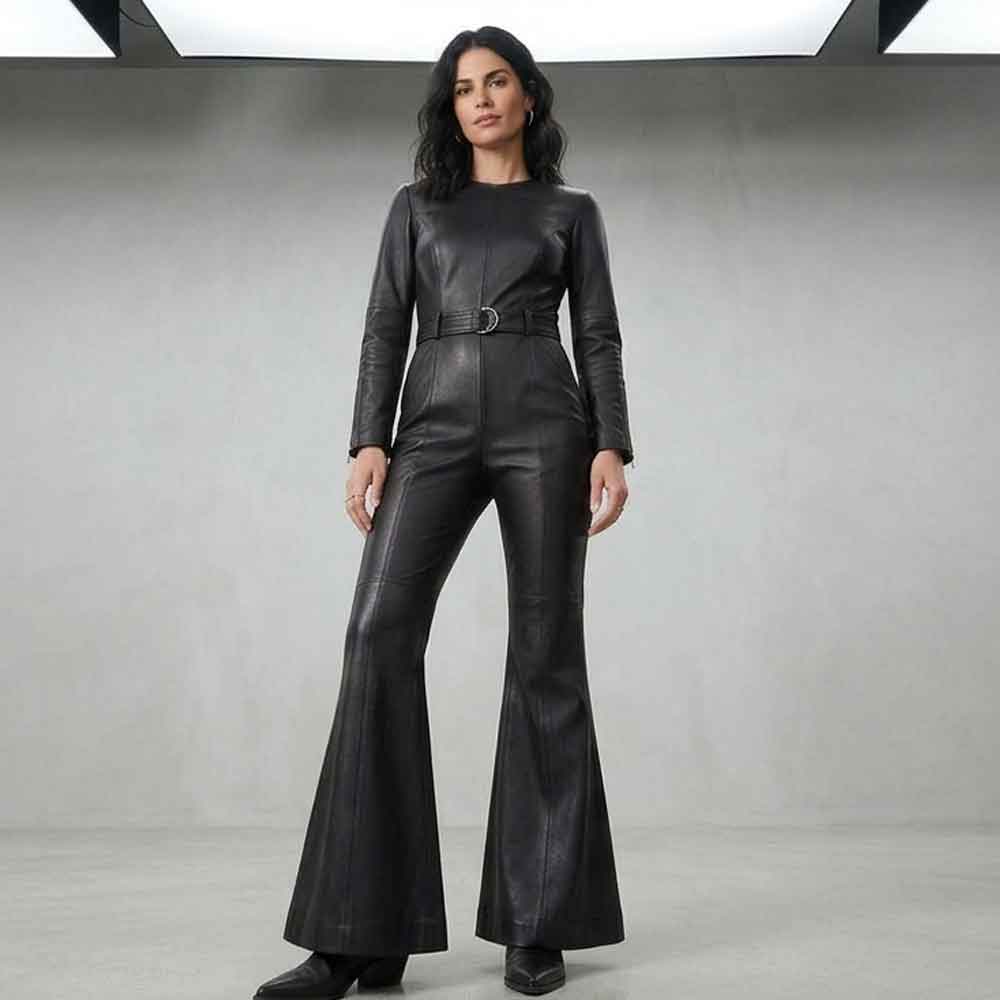 A woman modeling a black leather jumpsuit with long sleeves, a defined waist, and wide flared legs, standing against a gray studio backdrop.