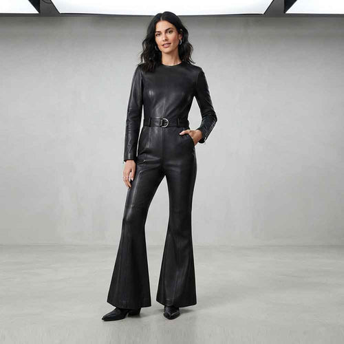 A woman modeling a black leather jumpsuit with long sleeves, a matching belt, and flared legs, standing in a studio with a light gray background.