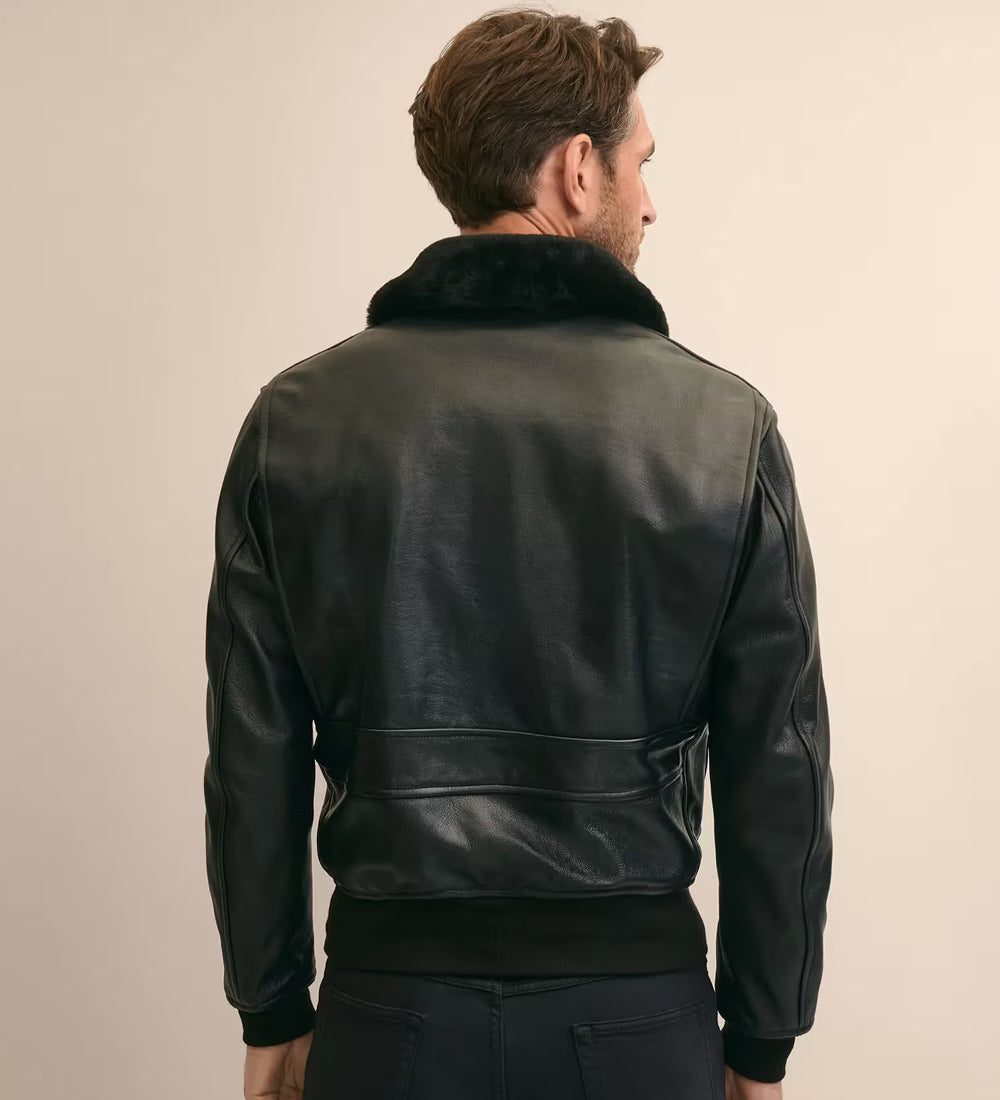 A man viewed from behind wearing a black leather jacket with a dark fur collar, set against a plain beige studio background.