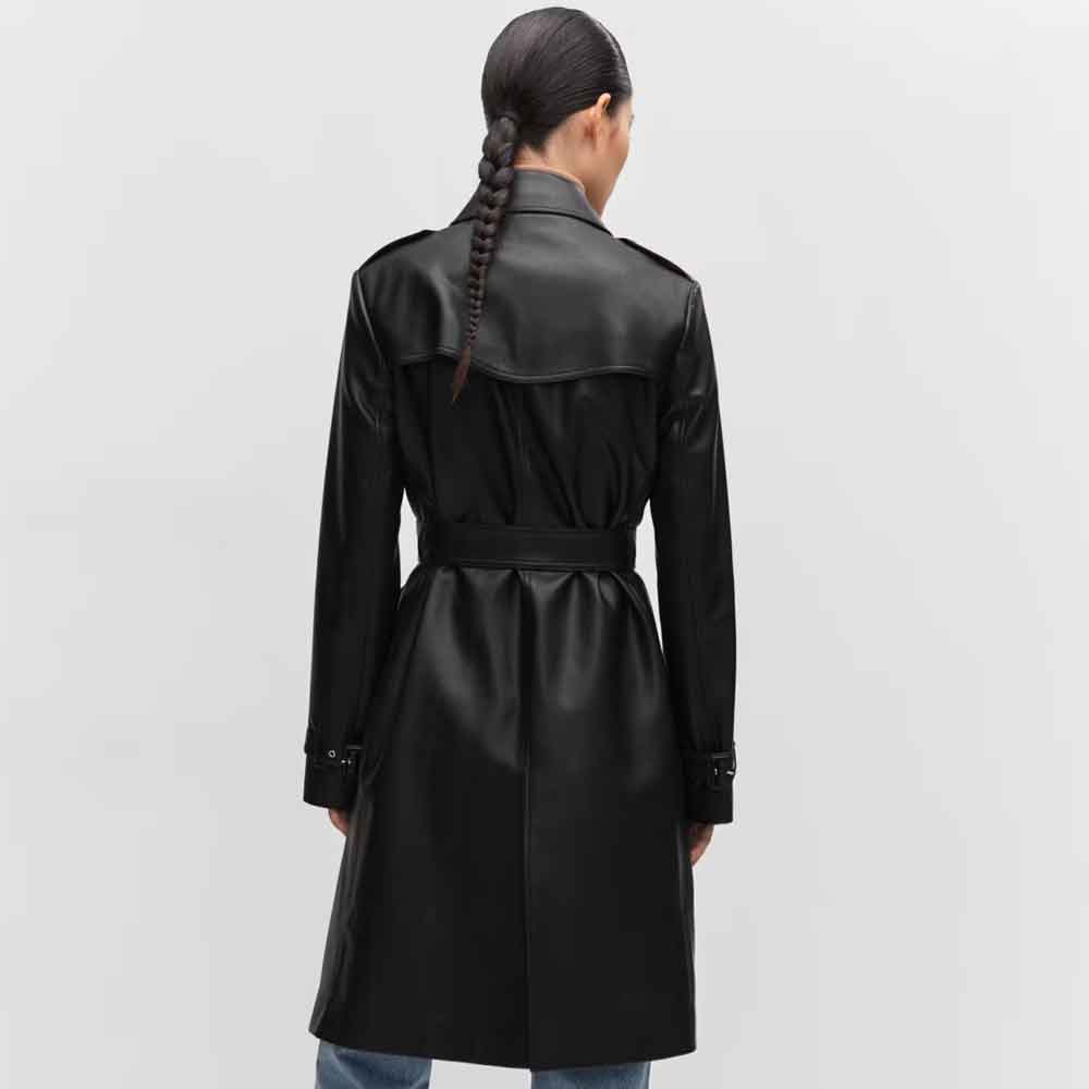 A woman viewed from the back wearing a black leather trench coat with a matching waist belt, set against a plain light gray studio background.