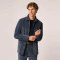 A man wearing a dark Blue Corduroy Jacket and matching corduroy trousers over a black t-shirt and brown belt, standing against a light gray studio background.