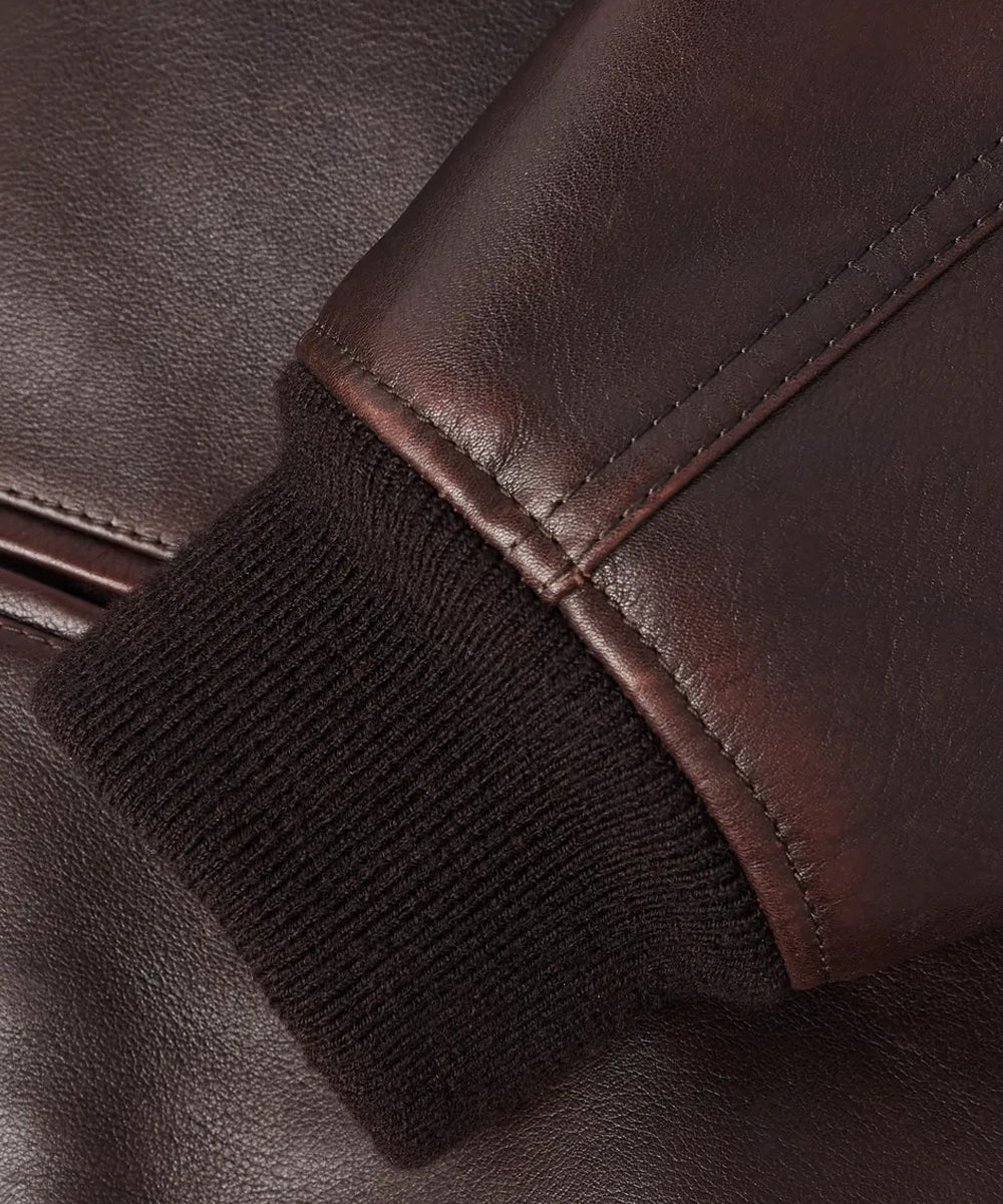 Close-up detail of a dark brown leather jacket sleeve with a ribbed black knit cuff, showing the texture and stitching.