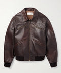 A dark brown Designer Leather Bomber Jacket with a front zipper, zippered chest pockets, and ribbed knit collar, cuffs, and hem, displayed on a light gray background.