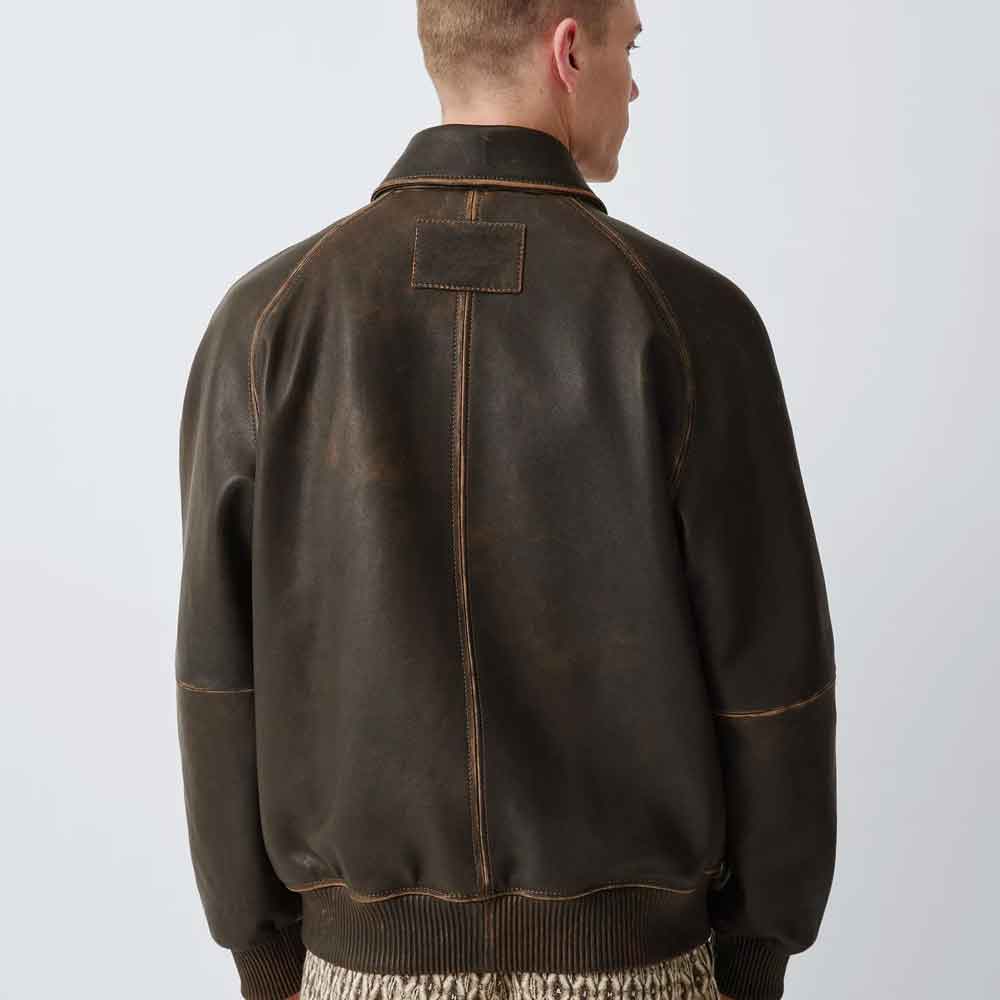 A man shown from the back wearing a dark brown distressed leather jacket with tan contrast stitching, set against a plain light gray studio background.