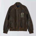 A Embroidered Bomber Jacket with a distressed finish, featuring a light beige embroidered graphic on the left chest and contrast stitching, shown against a light gray background.