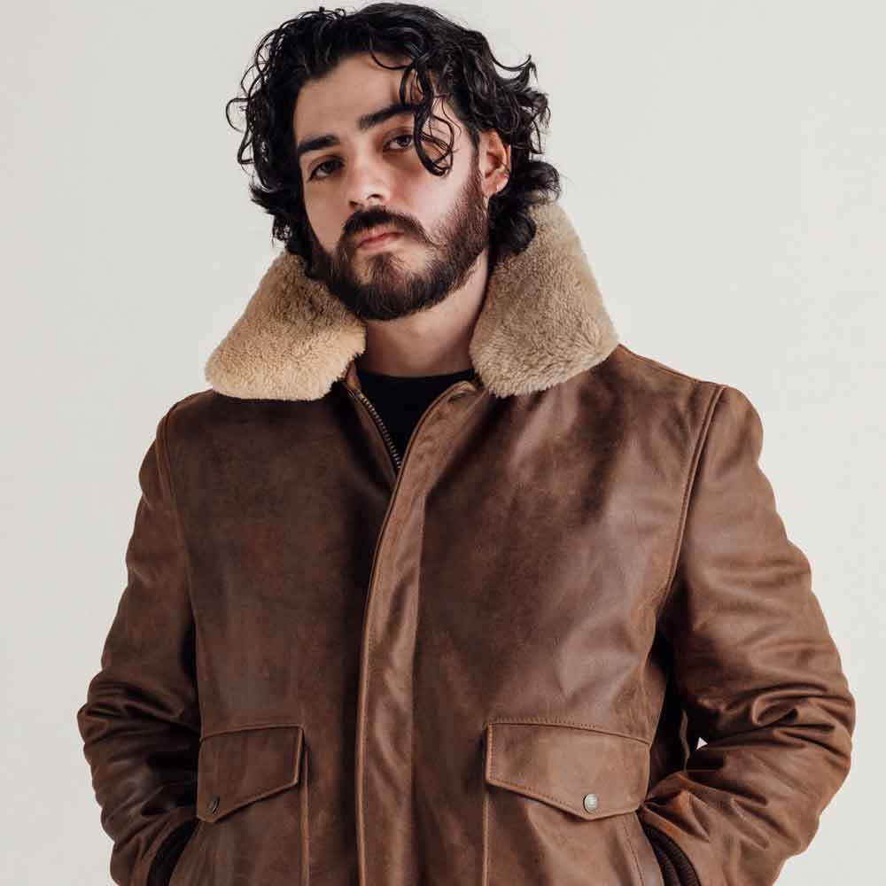 A man wearing a brown leather jacket with a thick beige shearling-style collar, photographed against a plain light background.