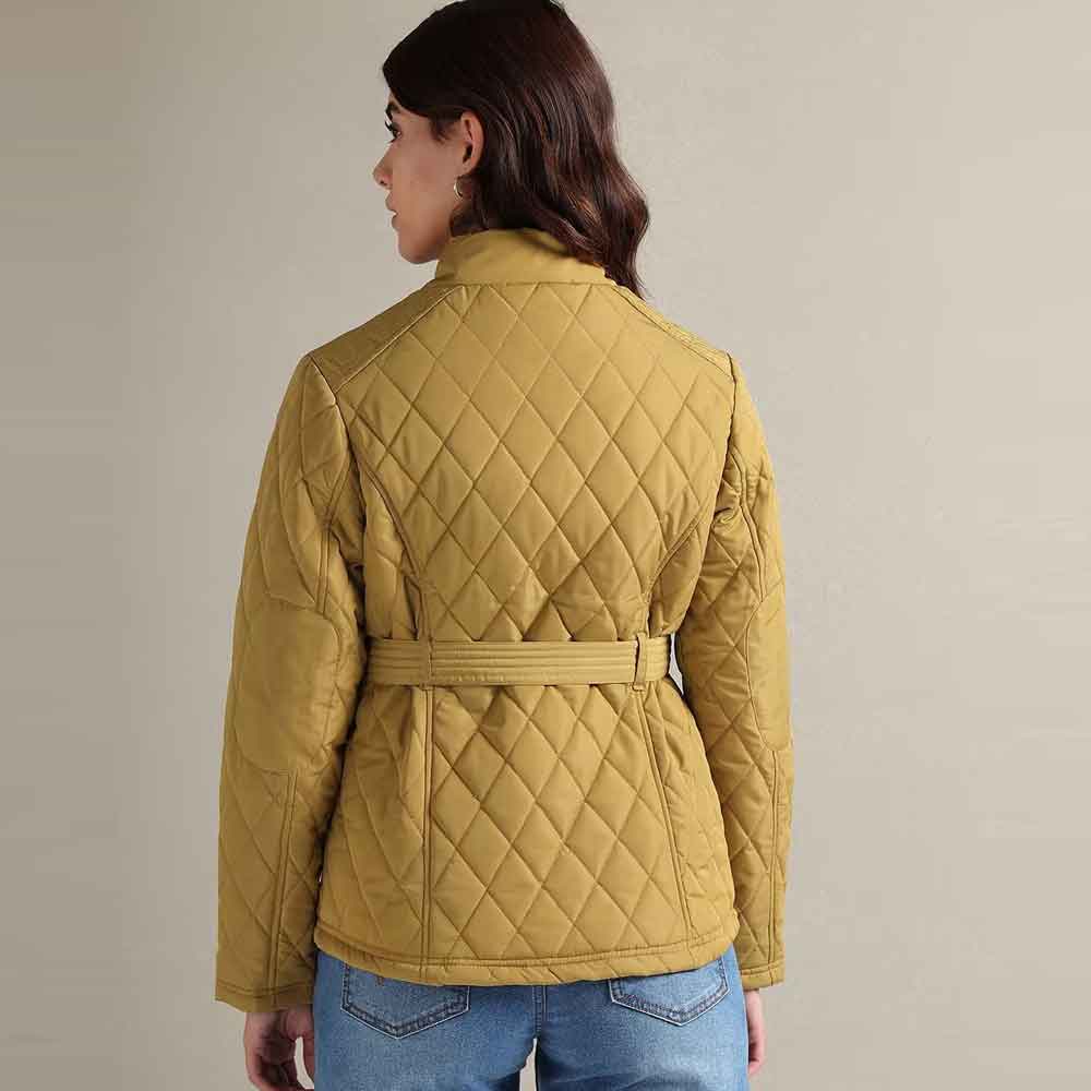 A woman shown from the back wearing a mustard yellow quilted jacket with a matching waist belt, paired with blue jeans, against a plain light gray studio background.