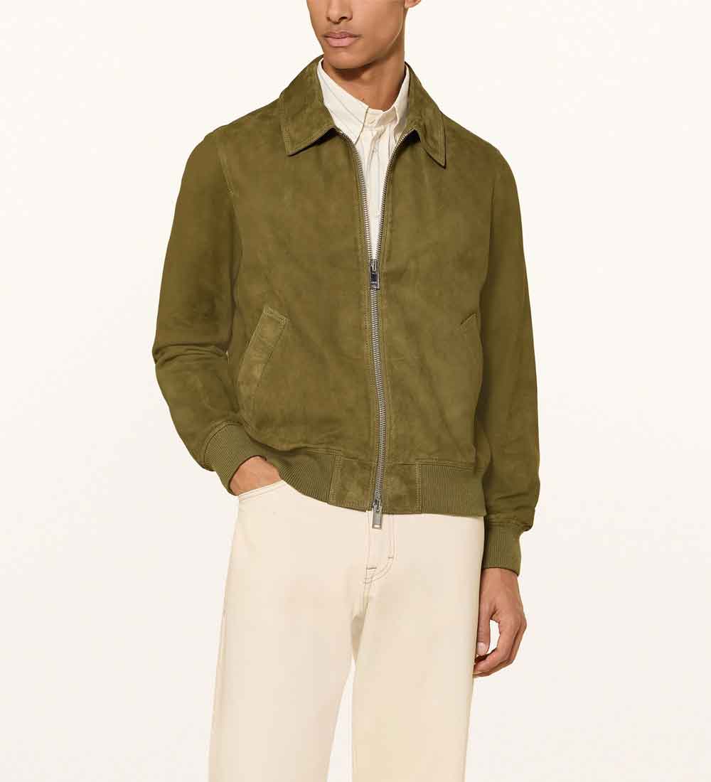 A man wearing an olive green suede zip-up jacket over a white collared shirt and cream trousers, photographed against a clean off-white studio background.