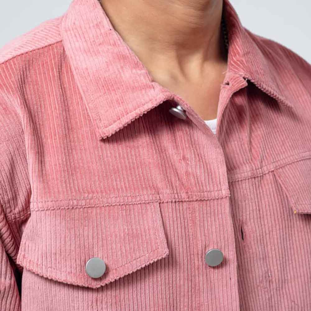 Close-up of a pink corduroy jacket with a pointed collar, buttoned front, and flap chest pockets with silver snap buttons, worn by a model.