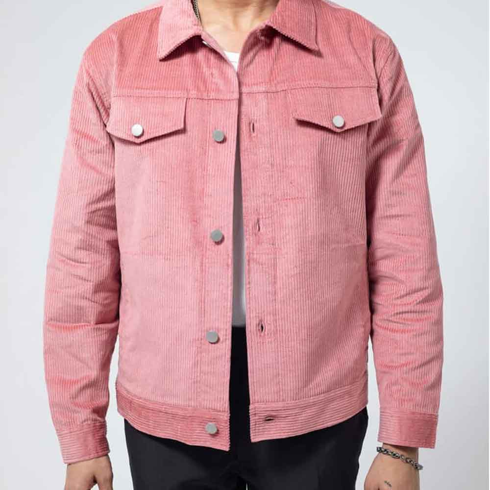 A pink corduroy trucker jacket with silver buttons, worn by a model over a white t-shirt and black pants, shot against a light gray background.