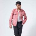 A man wearing a dusty Pink Corduroy Jacket over a white t-shirt and black trousers, standing against a light gray studio background.