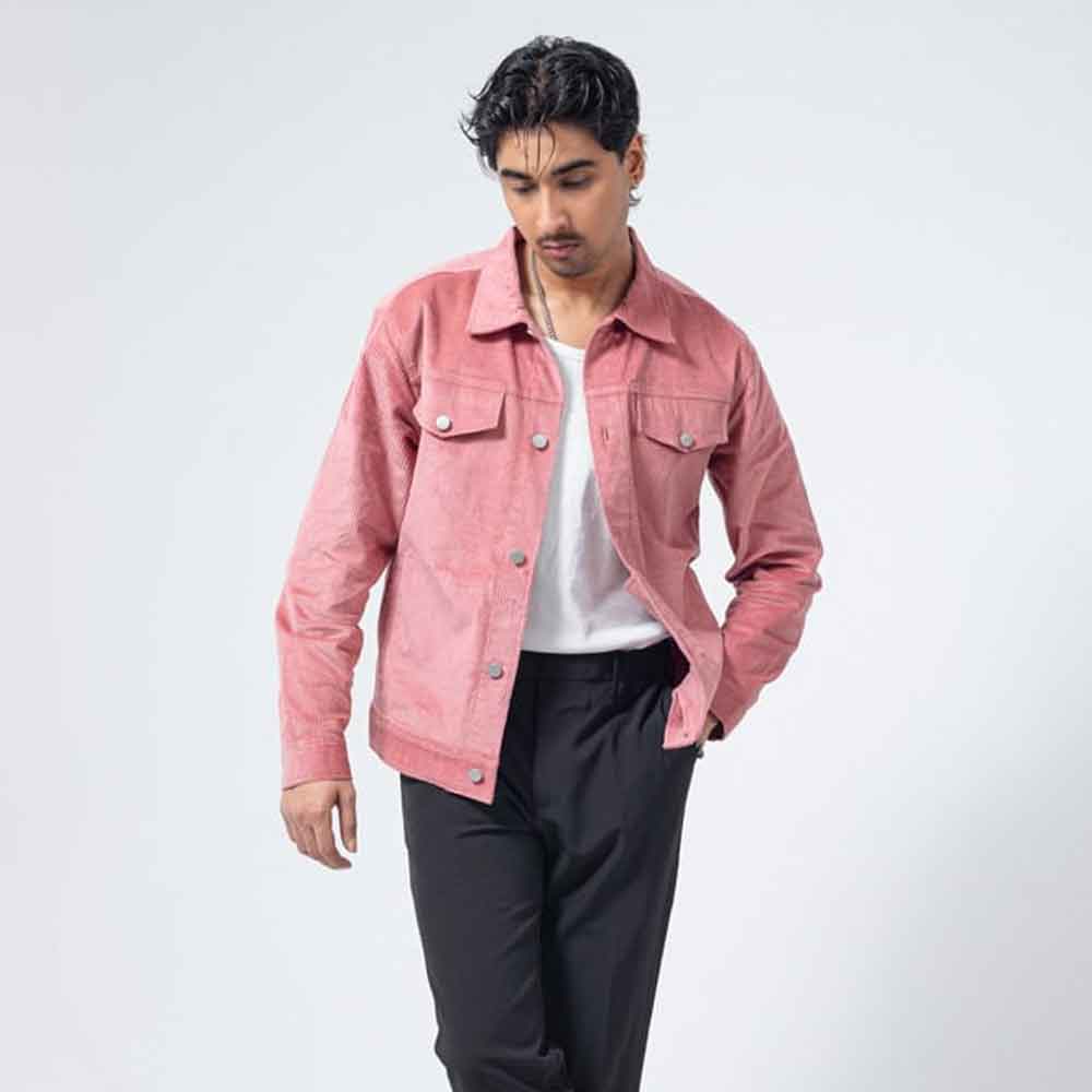 A man wearing a dusty Pink Corduroy Jacket over a white t-shirt and black trousers, standing against a light gray studio background.