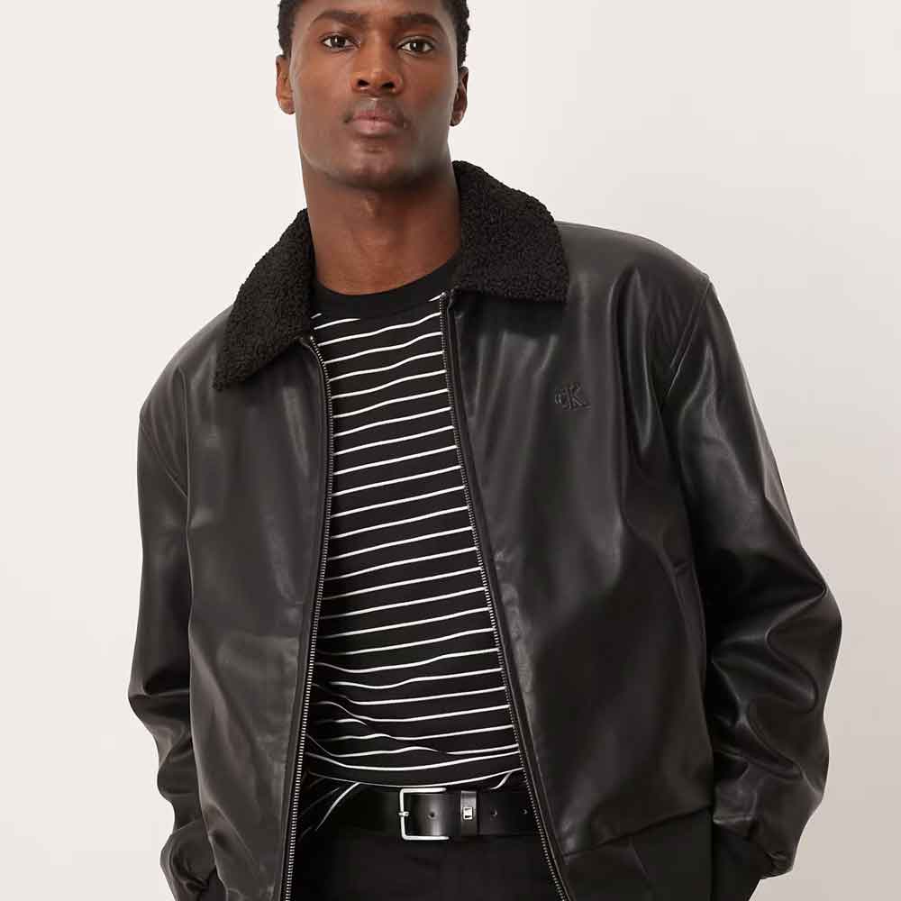 A man wearing a black leather bomber jacket with a black sherpa collar, layered over a black and white striped t-shirt.