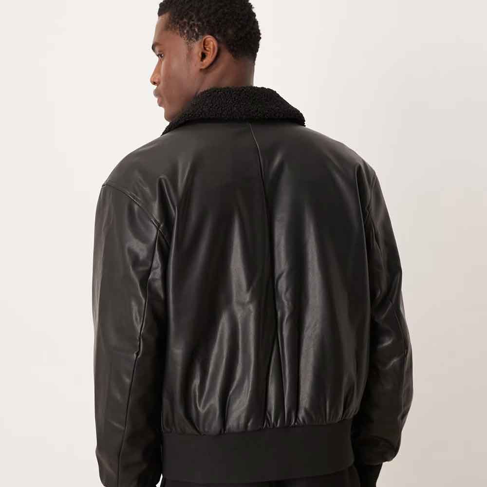 A man viewed from the back wearing a black leather bomber jacket with a black sherpa collar, set against a plain light gray studio background.