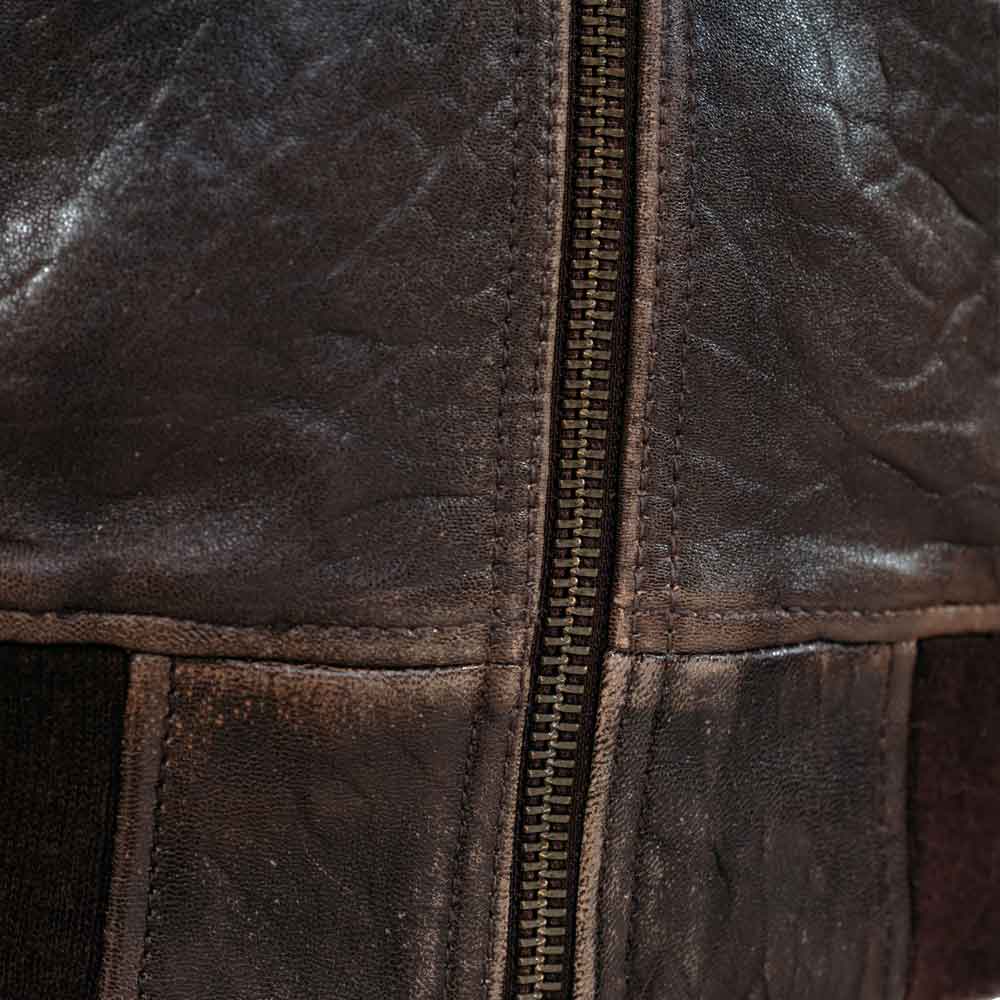 Close-up of a distressed dark brown leather jacket with a central metal zipper and visible stitching.
