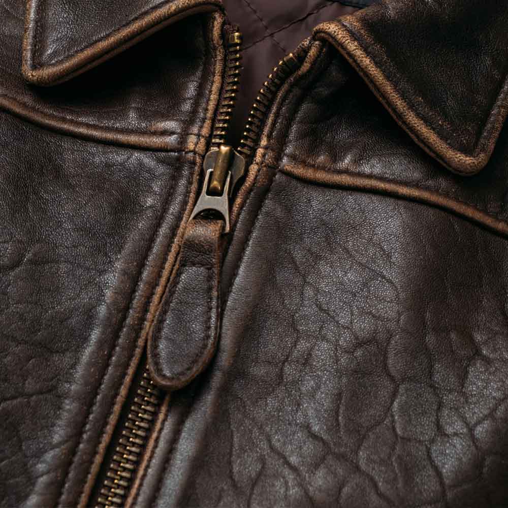 Close-up of a dark brown textured leather jacket with a front zipper, showing the collar, stitching, and leather grain detail.