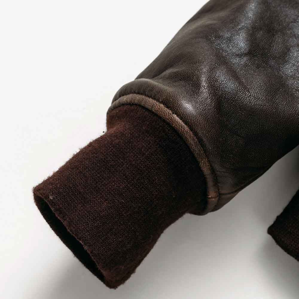 Close-up of a dark brown leather sleeve with a ribbed knit cuff in a matching dark brown color, shown on a light gray background.