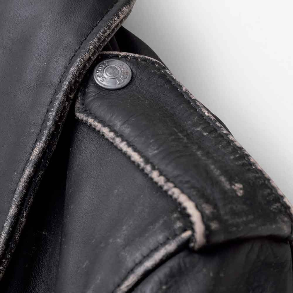 Close-up detail of a black leather jacket showing a silver metal snap button on the shoulder with contrast stitching.
